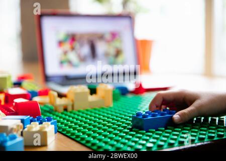 Girl playing with constructor at home, watching teacher's online tutorial on laptop. Digitalization, remote education concept. Technologies and devices. Man showing, giving online lesson. Artwork. Stock Photo