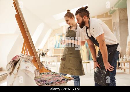 Warm-toned side view portrait of creative couple painting picture together and smiling while standing by easel in art studio, copy space Stock Photo