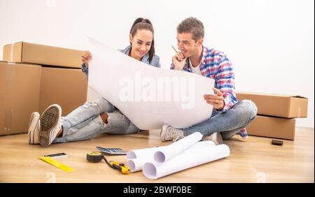 Happy couple moved into a new house  discussing the interior design over blueprints. Stock Photo