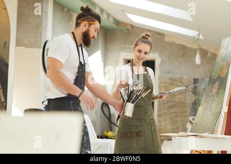 Portrait of creative young couple painting picture together while enjoying work in art studio, copy space Stock Photo