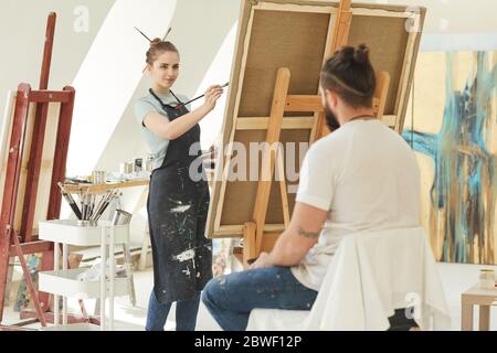 Portrait of young female artist painting portrait of man in studio, copy space Stock Photo
