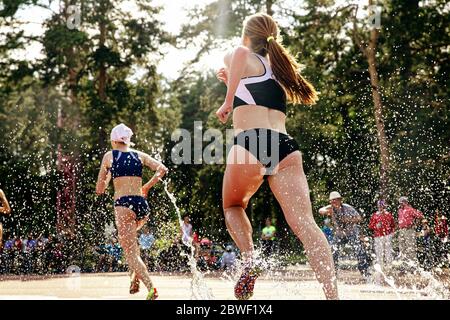 back two girl athletes runners run steeplechase splashes and drops of water Stock Photo