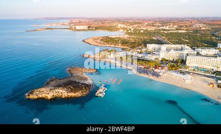 Aerial bird's eye view of famous Nissi beach coastline, Ayia Napa, Famagusta, Cyprus. The landmark tourist attraction islet bay at sunrise with golden Stock Photo