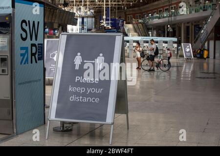 Face Covering and hand washing hygiene requesting signs stand within the Waterloo main station concourse, London, England, UK Stock Photo