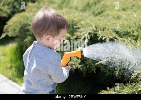 Small boy with watering can watering trees on backyard. Happy childhood concept Stock Photo