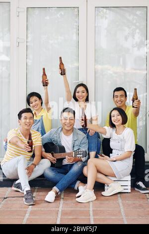 Hands young man playing guitar when his happy friends raising hands with bottles of beer Stock Photo