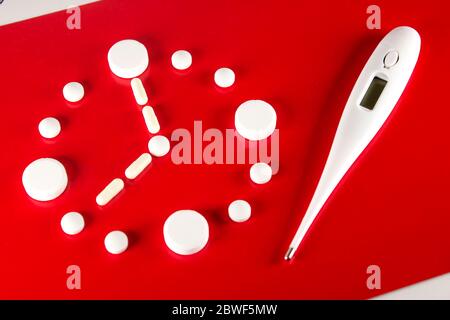 Clock made of white tablets and thermometer on red background, top view. 2019 Novel Coronavirus 2019-nCoV concept Stock Photo