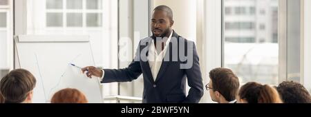 Confident African business coach gives presentation on flipchart to staff Stock Photo