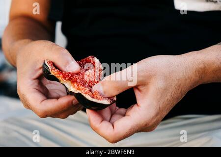 closeup of a caucasian man outdoors, in casual wear, opening a fig with his hands Stock Photo