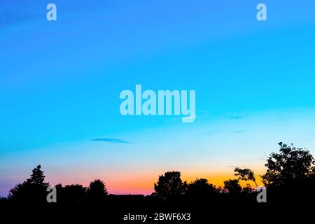 An orange sunset against a blue sky in the shade of trees Stock Photo