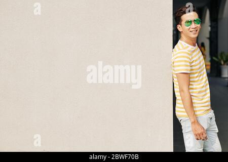 Handsome young Asian man in sunglasses leaning on  and smiling at camera Stock Photo