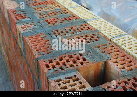 An exhaust shaft in a wall of red brick filled with cement. Facing with yellow and brown bricks. Selective focus. onstruction concept. Unfinished hous Stock Photo