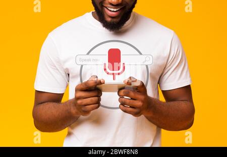 African Guy Using Voice Search On Smart Phone, Yellow Background Stock Photo