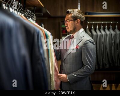 Young handsome man in costume looking for jacket in shop Stock Photo