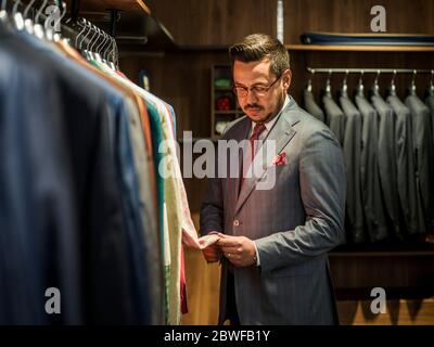 Young handsome man in costume looking for jacket in shop Stock Photo