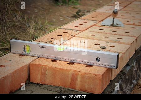 Row of Red Bricks on a Wall. Selective focus. Red bricks on top of a wall, spatula, red brick masonry, construction concept. Trowel and bricks lying o Stock Photo