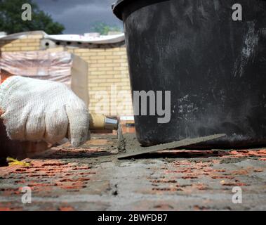 Bricklayers hands with in masonry trowel bricklaying new house wall on foundation. Close up of industrial bricklayer installing bricks. Bricklayer and Stock Photo