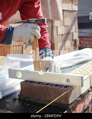 Bricklayers hands with in masonry trowel bricklaying new house wall on foundation. Close up of industrial bricklayer installing bricks. Bricklayer and Stock Photo