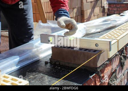 Bricklayers hands with in masonry trowel bricklaying new house wall on foundation. Close up of industrial bricklayer installing bricks. Bricklayer and Stock Photo