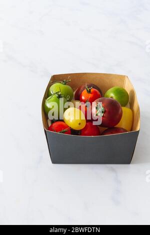 Small cardboard box of heirloom cherry tomatoes on a white marble backdrop Stock Photo