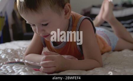 child boy watch play smartphone on bed at home wearing nappies. distance learning education Stock Photo