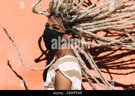Portrait of african girl moving blond dreadlocks hair wearing face protective mask for Coronavirus prevention - Covid 19 lifestyle and trendy people c