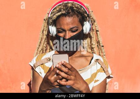 Yound african woman with blond dreadlocks using mobile phone while listening playlist music - Trendy person having fun with technology trends - Tech, Stock Photo