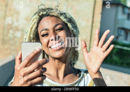 Yound african woman with blond dreadlocks doing video call with smart mobile phone - Trendy person having fun with technology trends - Tech, lifestyle Stock Photo