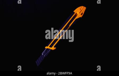 Orange cutter knife isolated on a black background.  Very sharp knife to work on the cardboard and thin sheets of plastic Stock Photo