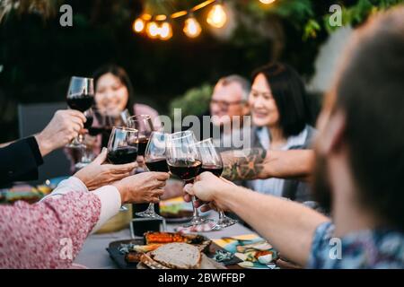 Happy family cheering with red wine at barbecue dinner outdoor - Different age of people having fun at weekend meal - Food, taste and summer concept - Stock Photo