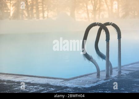 Warm swimming pool hand rail in frosty weather, outdoor, soft focus on stainless steel stair railing covered with ice. Stock Photo