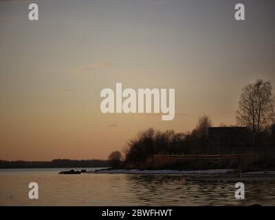 Wooden house on the river. Sunset, spring. House on the river with sunset view. Evening sunrise on a choppy river wind early spring landscape. Sunset Stock Photo