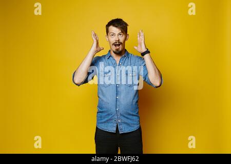 Young guy with beard and mustache pointing finger and looking in the camera, isolated over yellow background. Young emotional hipster Stock Photo