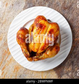 whole roast chicken served on a white plate on a stone table, flat lay, close-up Stock Photo