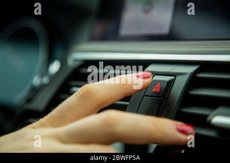 a female finger press the emergency light button on the dashboard of a car. close-up, soft focus, in the background car interior details in blur, side Stock Photo