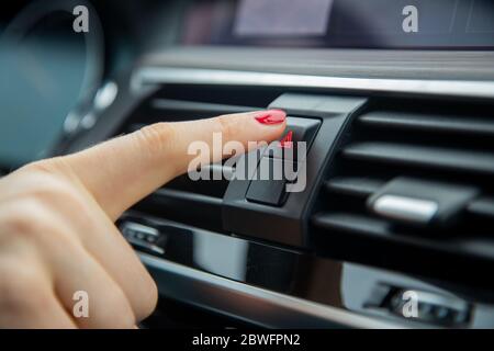 a female hand press the alarm light button on the dashboard of a car. close-up, soft focus, in the background car interior details in blur, side view Stock Photo