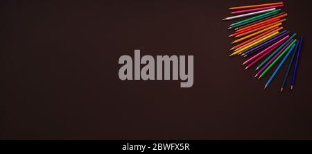 colour pencils on brown background, back to school concept. Stationeries on blackboard. Banner format. Top view Stock Photo