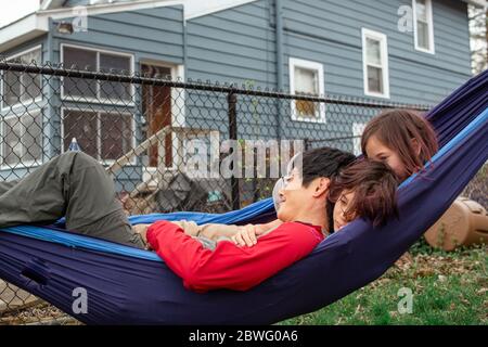 Two happy children snuggle their father in a hammock in their backyard Stock Photo