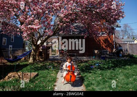 a child sits under flowering magnolia tree in backyard playing cello Stock Photo