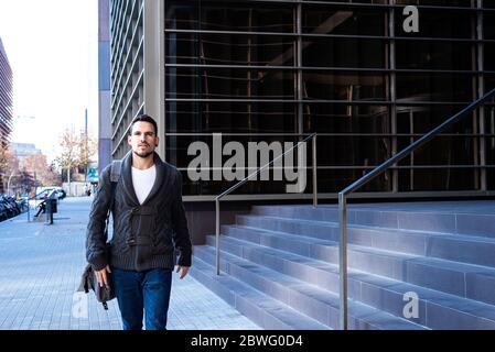 Young bearded man walking on the street next to office building Stock Photo