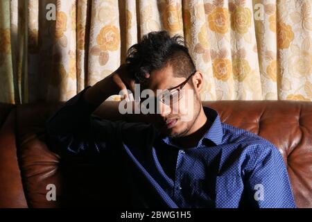 Sad young man in casual dress sitting on sofa. Stock Photo
