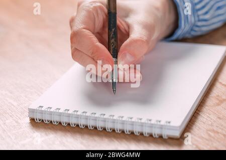 Close up of woman's hands writing in spiral notepad placed on wooden desktop Stock Photo