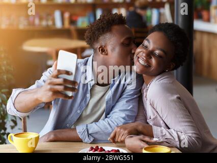 African American man taking selfie while kissing his girlfriend at urban cafe Stock Photo
