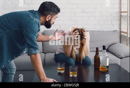 Drunken scandal. Woman holds her head and sitting on sofa, angry man