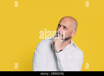 Handsome serious middle aged man meditate on yellow background Portrait of a senior man who thinks and holds a hand near his face leaning against a ye Stock Photo