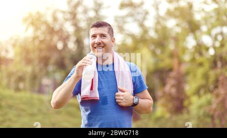 Sweaty mature jogger man drinking water after jogging Stock Photo