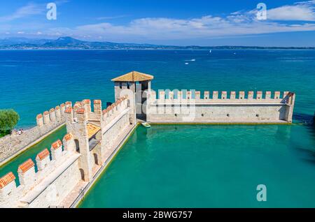 Sirmione, Italy, September 11, 2019: Small fortified harbor with turquoise water, Scaligero Castle Castello fortress, town on Garda lake, medieval castle with stone towers and brick walls, Lombardy Stock Photo