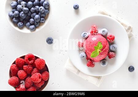 Raspberry sorbet on plate and fresh berries in bowl on light stone background. Top view, flat lay Stock Photo