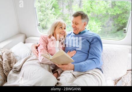 Loving mature couple reading book on bed in camper van during family trip Stock Photo