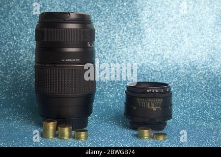 Cheap and old manual lens versus expensive lens with autofocus on a blue background with coins denoting the value of the lenses. Stock Photo